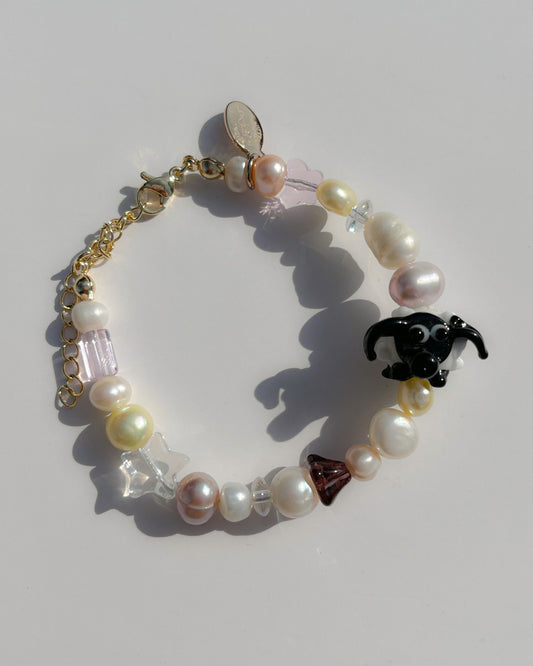 A studio shot of Buttercup Studio's Little Bo Peep Freshwater Pearls Bracelet. Made with assorted pink, yellow and white freshwater pears, clear beads, a brown mushroom cap bead and a special black and white sheep lampwork glass bead.