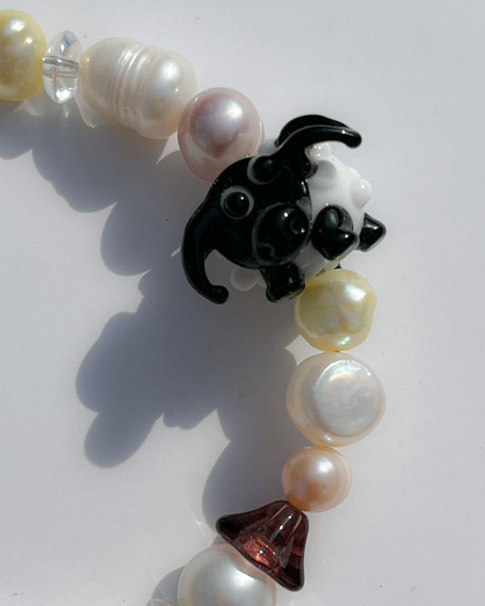 A close up studio shot of Buttercup Studio's Little Bo Peep Freshwater Pearls Bracelet. Made with assorted pink, yellow and white freshwater pears, clear beads, a brown mushroom cap bead and a special black and white sheep lampwork glass bead.