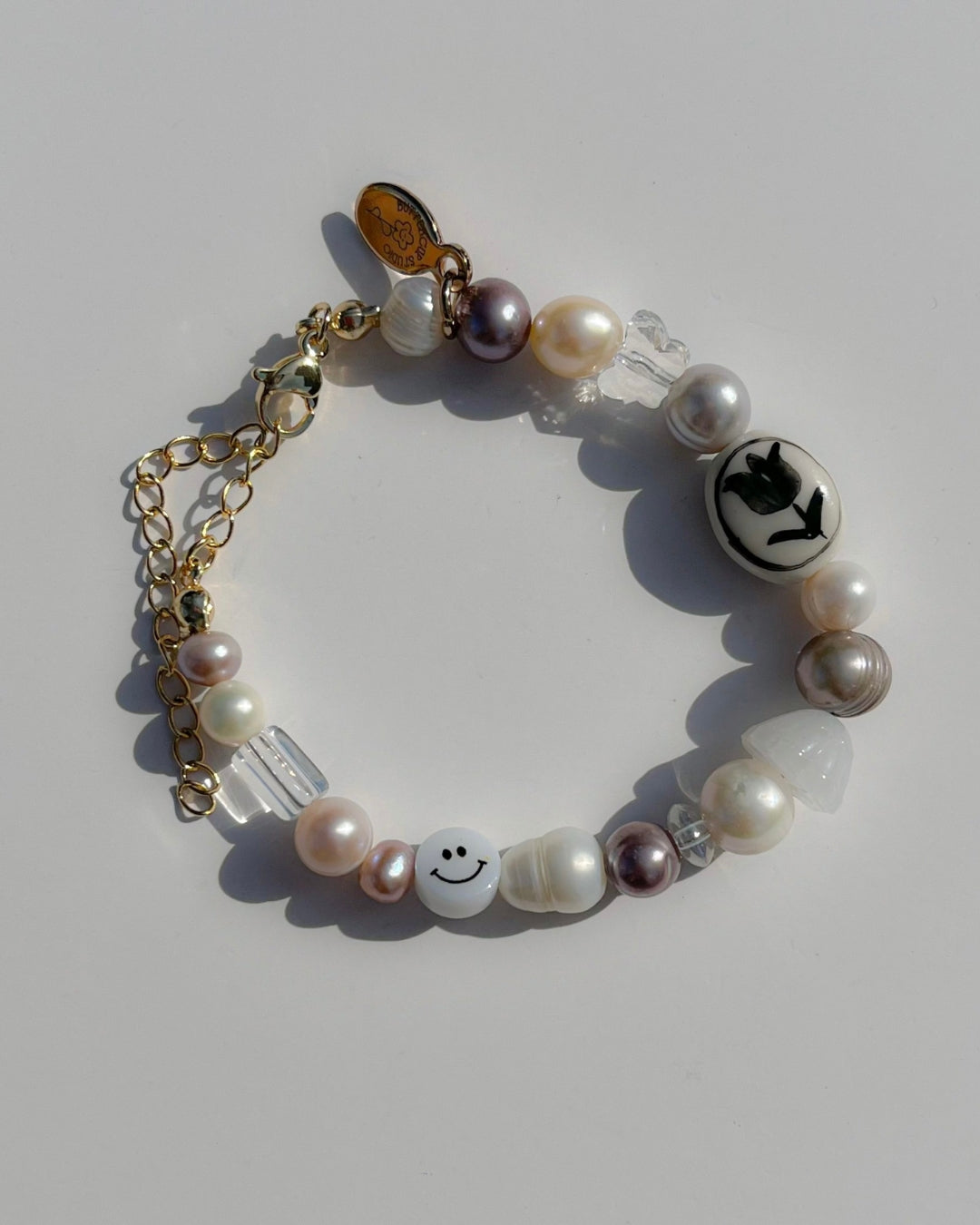 A studio shot of Buttercup Studio's Painter Tulip Freshwater Pearls Bracelet. Made with assorted freshwater pearls, clear and white beads, a white smiley face bead and a special lampwork white glass bead with a black hand-painted tulip.