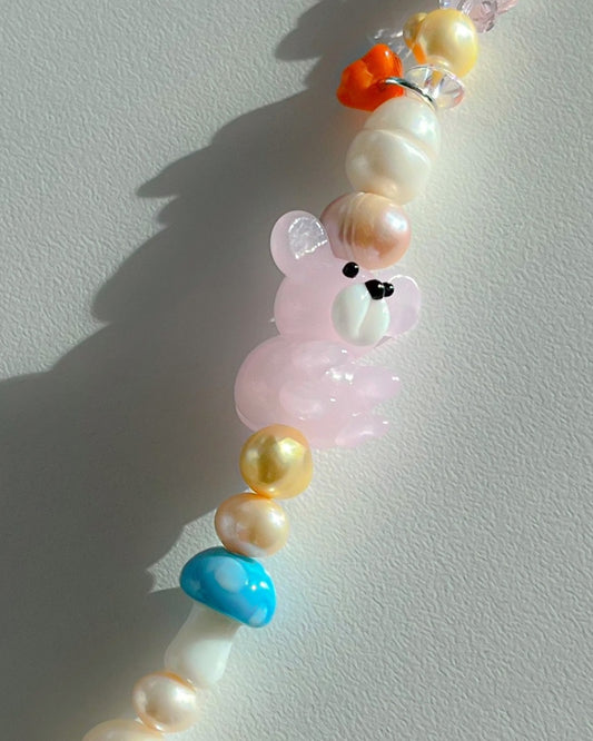 A close up studio shot of Buttercup Studio's Pink Forest Teddy Freshwater Pearls Bracelet. Made with assorted freshwater pearls, green, yellow, orange and pink charms, a special lampwork blue mushroom glass bead and a special pink teddy lampwork glass bead.