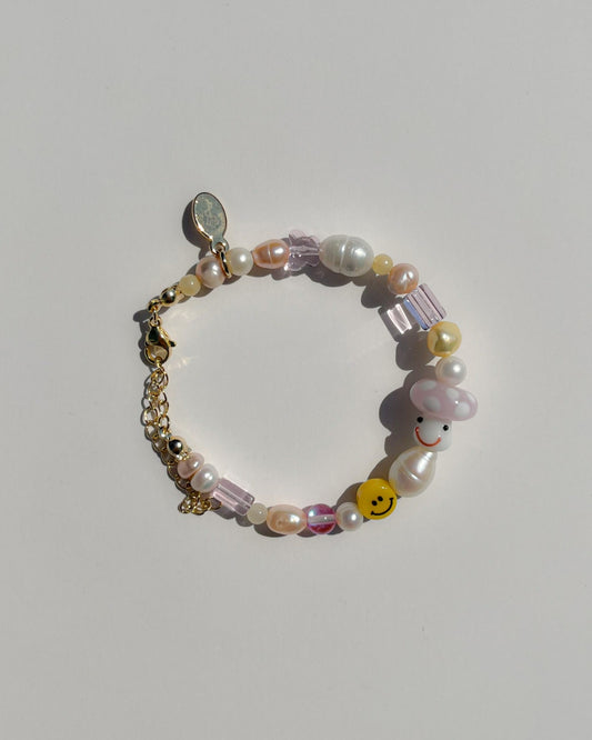 A studio shot of Buttercup Studio's Pink Shroomie Freshwater Pearls Bracelet. Includes assorted freshwater pearls, sheer pink beads, a yellow smiley face bead and a special lampwork glass pink mushroom bead. 