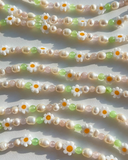 Close up studio shot of multiple Daisy For You Freshwater Pearls Bracelets by Buttercup Studio. Features freshwater pearls in assorted colours and sizes, green beads and daisy charms.
