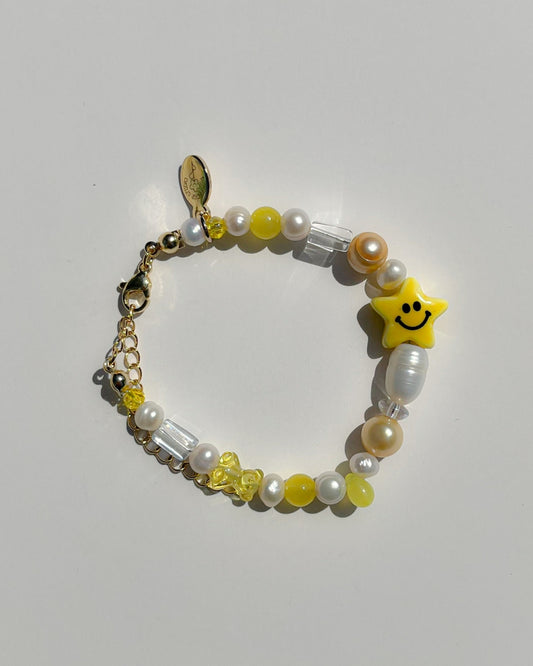 A studio shot of Buttercup Studio's Shooting Star Freshwater Pearls Bracelet. Made with assorted freshwater pearls, yellow and white beads, and a special lampwork glass smiley face star bead. 
