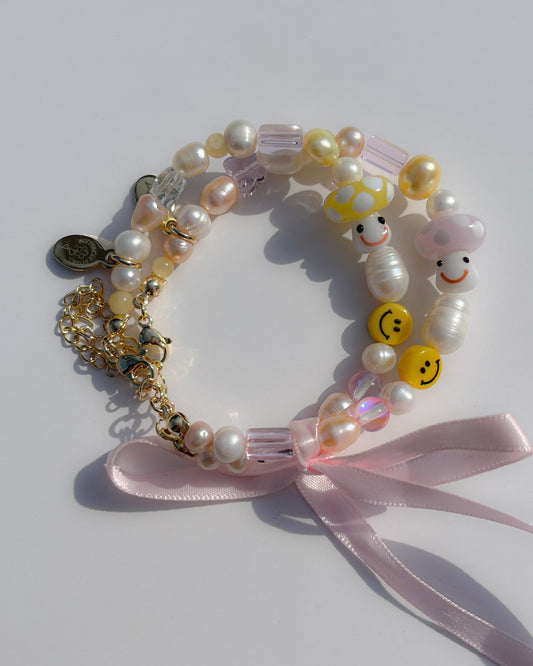 Both the Pink Shroomie Freshwater Pearls Bracelet and the Yellow Shroomie Freshwater Pearls Bracelet on top of one another, tied together with a pink bow.