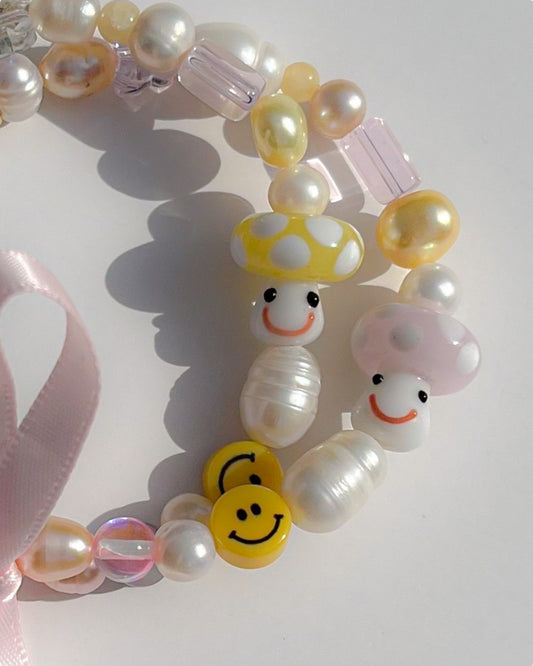 A close up shot of both the Pink Shroomie Freshwater Pearls Bracelet and the Yellow Shroomie Freshwater Pearls Bracelet on top of one another, tied together with a pink bow.