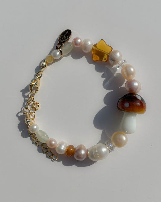 A studio shot of Buttercup Studio's Starry Mushroom Freshwater Pearls Bracelet. Made with assorted freshwater pearls, amber beads, and a special lampwork brown mushroom glass bead.