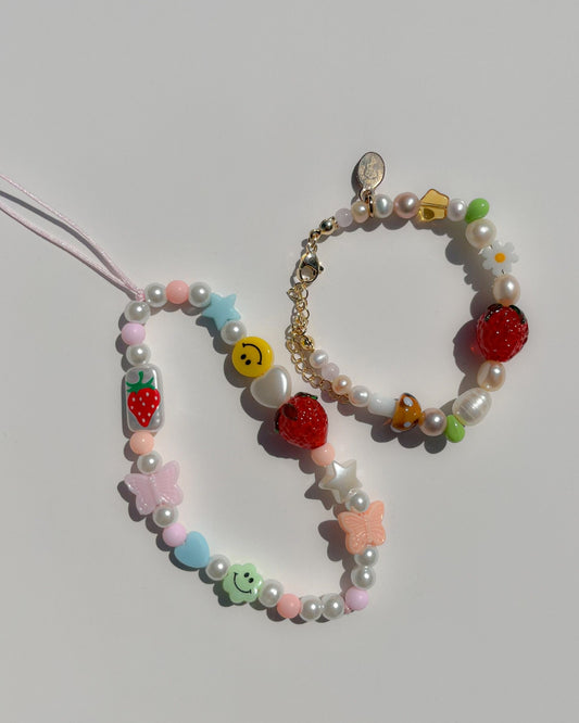 Buttercup Studio's Summertime Strawberry Freshwater Pearls Bracelet next to the Strawberry Jam Phone Strap. 