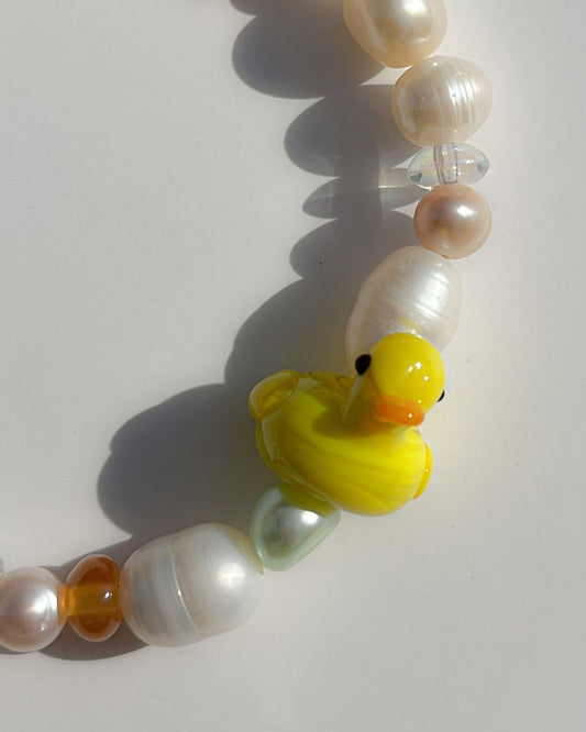 A close up studio shot of Buttercup Studio's Wonderland Duckie Freshwater Pearls Bracelet. Includes assorted freshwater pearls, orange and green beads, a lampwork glass pink mushroom bead and a yellow duck lampwork glass bead.