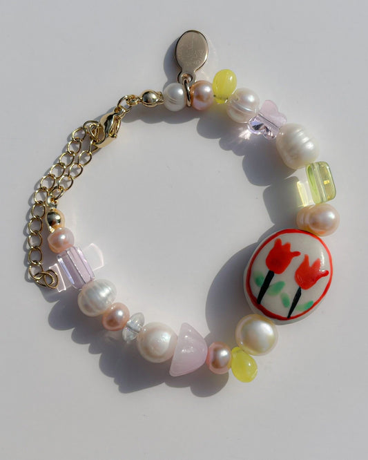 A studio shot of Buttercup Studio's Tulip Field Freshwater Pearls Bracelet. Made with assorted freshwater pearls, pink and yellow beads and a lampwork hand painted glass bead with two red tulips.