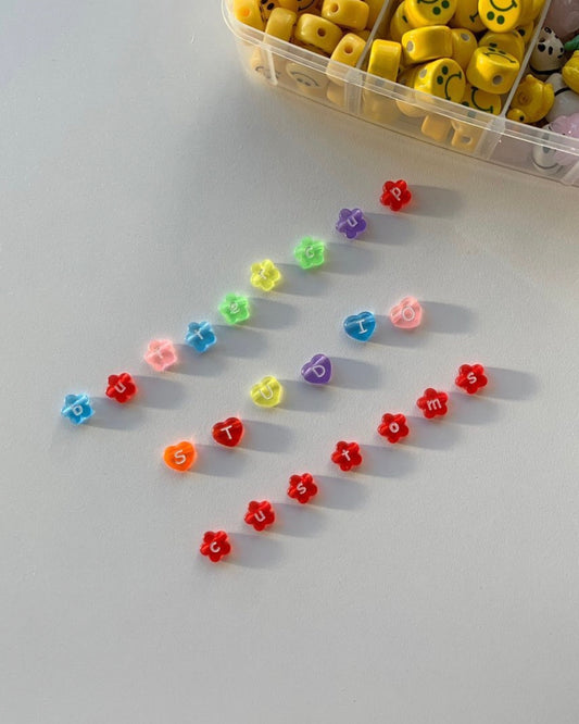 Assorted colourful flower shaped alphabet beads spelling "buttercup studio customs".