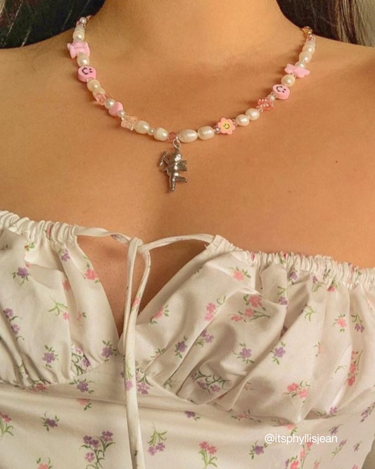 A close up of @itsphyllisjean on Instagram wearing a Custom Fairy Cherub Pendant Necklace by Buttercup Studio. Handmade with freshwater pearls, pink charms and a silver cherub in the center. 