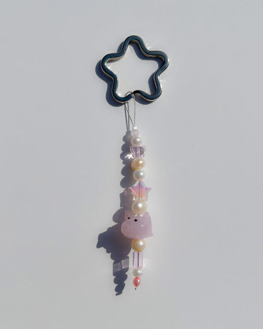 A studio shot of the one of one Baby Piglet Freshwater Pearls Lucky Charm keychain. Handmade using stainless steel wire looped on a star shaped keyring, this freshwater pearl keychain features white and yellow pearls, clear beads, sheer pink beads and a pink baby pig lampwork glass bead. 