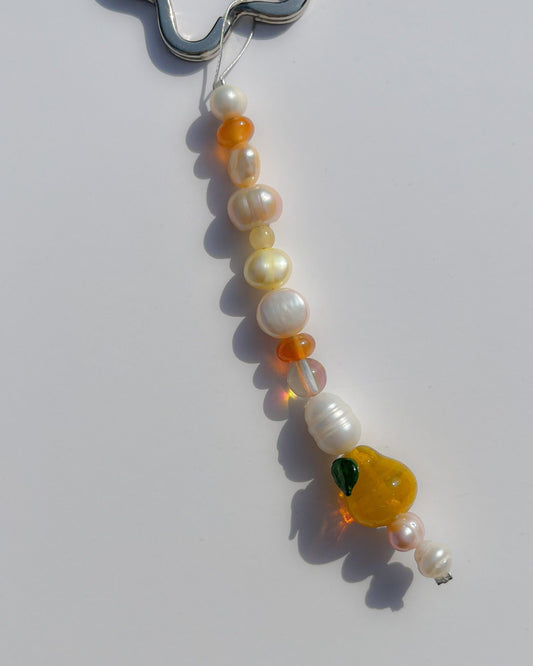 A close up studio shot of the one of one Citrine Amber Pear Freshwater Pearls Lucky Charm keychain. Handmade using stainless steel wire looped on a star shaped keyring, this freshwater pearl keychain features white, pink and yellow pearls, sheer orange beads, and a yellow pear lampwork glass bead. 
