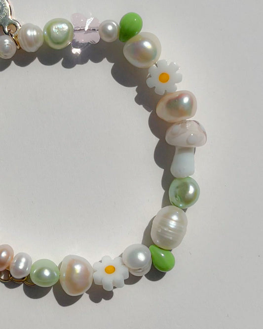 Close up studio shot of the Enchanted Freshwater Pearls Bracelet by Buttercup Studio. Features a white mushroom lampwork glass bead, daisy beads, green pearls and beads, and assorted freshwater pearls.