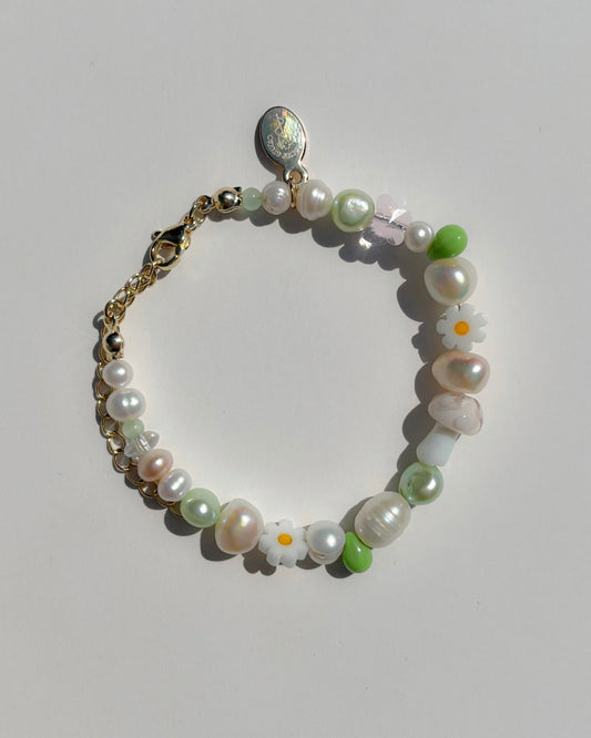 Studio shot of the Enchanted Freshwater Pearls Bracelet by Buttercup Studio. Features a white mushroom lampwork glass bead, daisy beads, green pearls and beads, and assorted freshwater pearls.