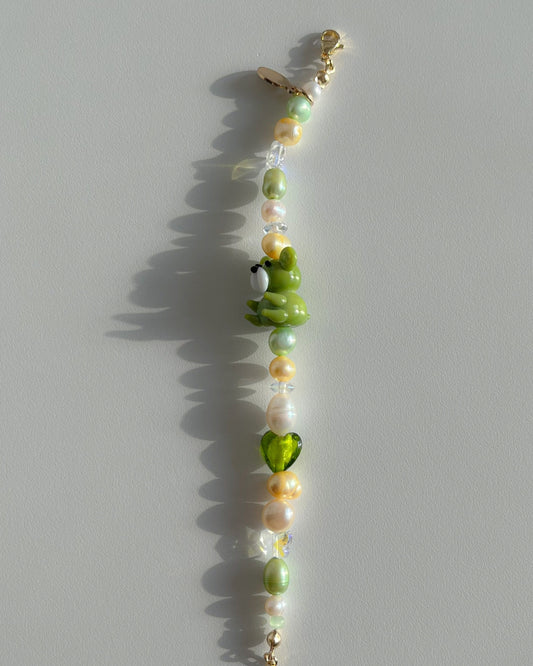 A studio shot of Buttercup Studio's Forest Teddy Freshwater Pearls Bracelet. Features clear beads, a sheer green heart bead, assorted yellow, green and white freshwater pearls, and a special green teddy lampwork glass bead.
