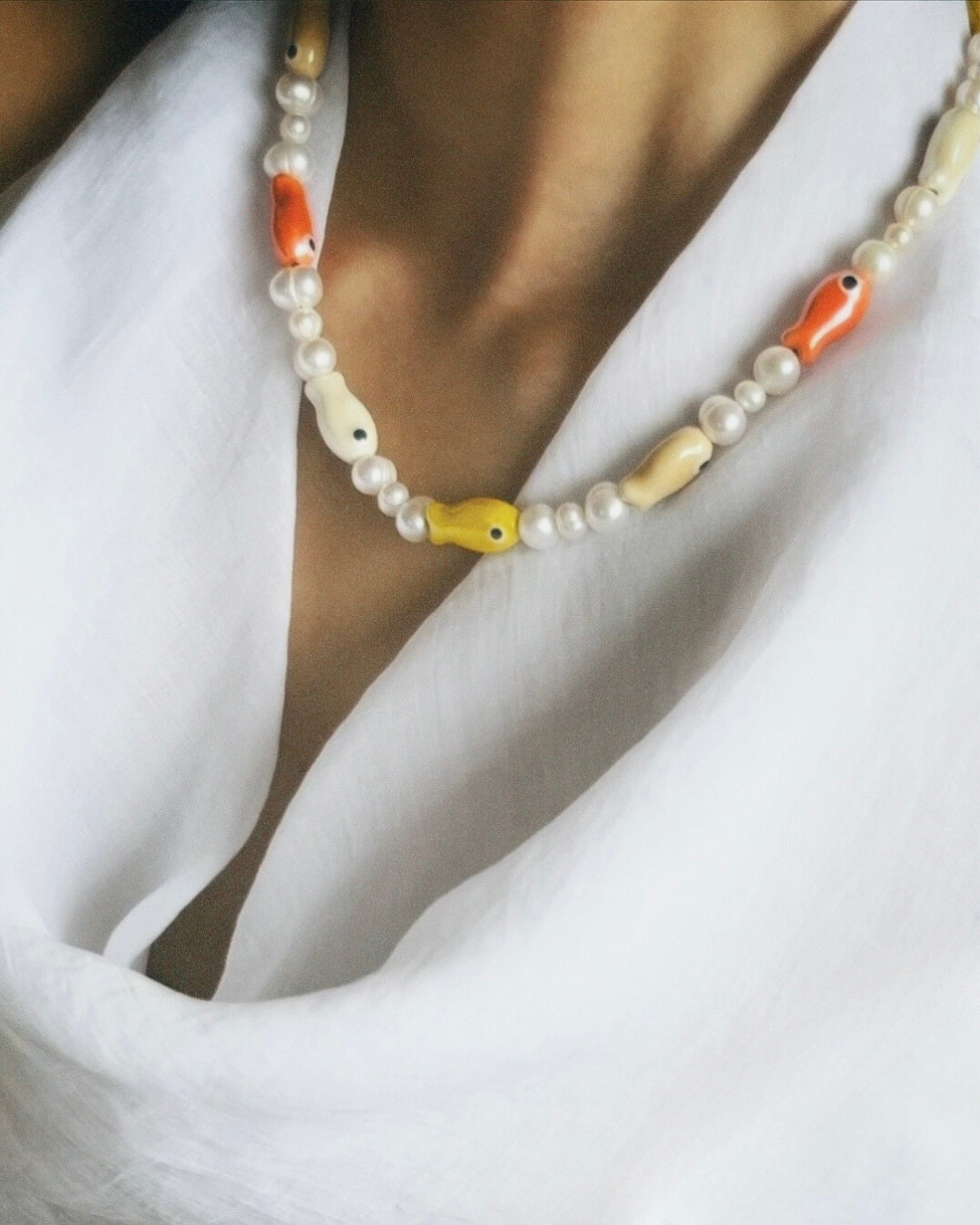 A close-up model shot of The Lucky Fish Freshwater Pearl Necklace is made using high quality rare AA+ freshwater pearls and glazed multi fish ceramic fish beads. Finished with 14k gold clasps and adjustable chain. This exclusive Buttercup Studio item is a limited edition and unisex.
