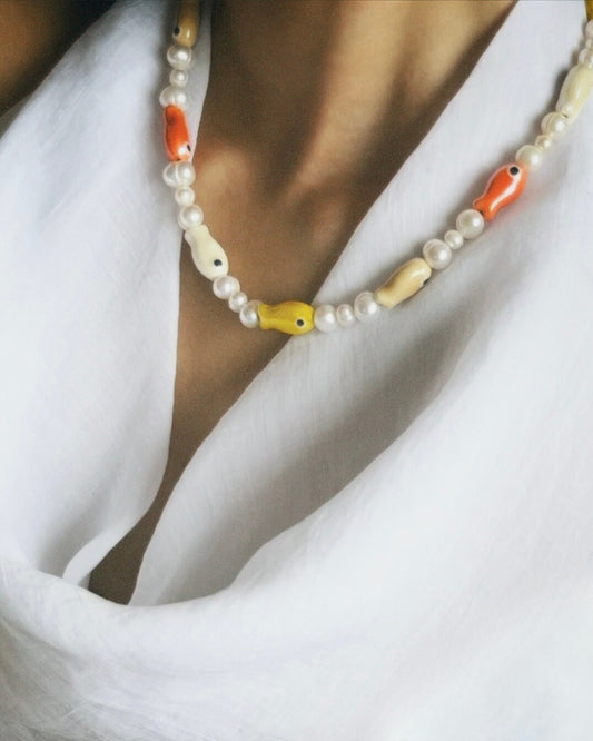 A close-up model shot of The Lucky Fish Freshwater Pearl Necklace is made using high quality rare AA+ freshwater pearls and glazed multi fish ceramic fish beads. Finished with 14k gold clasps and adjustable chain. This exclusive Buttercup Studio item is a limited edition and unisex. 