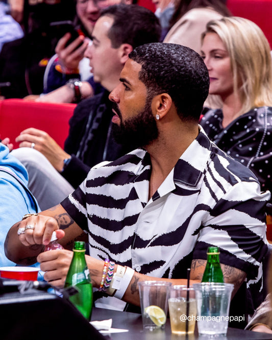 Drake seated at a sports event wearing a Custom Multi Colour Bracelet by Buttercup Studio. Image credits @champagnepapi on Instagram.