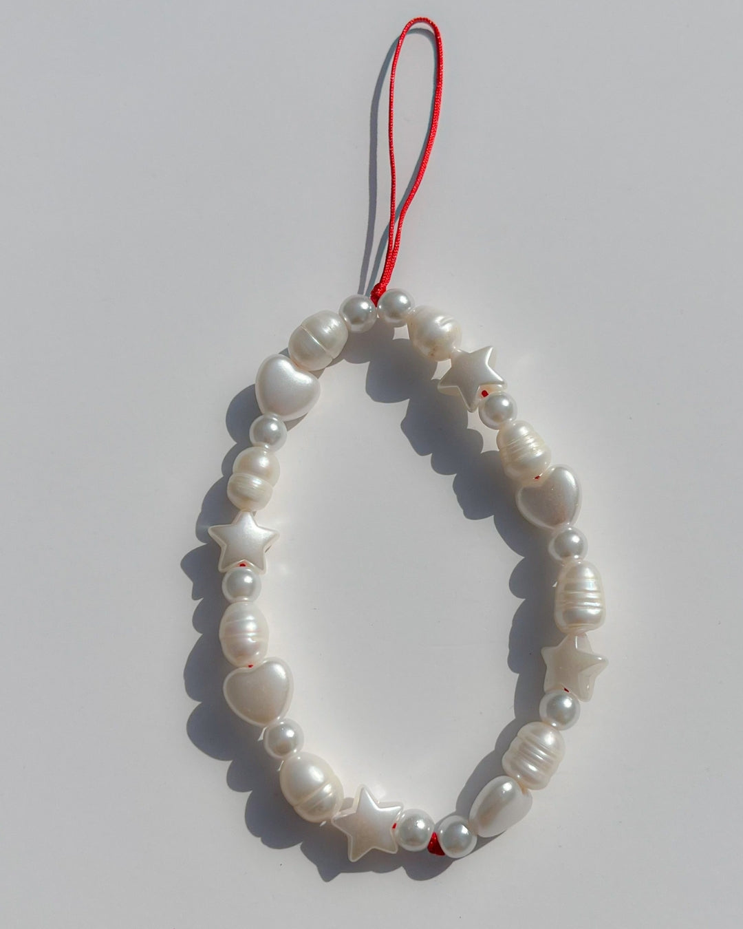 A studio shot of Buttercup Studio's Love Is In The Air Phone Strap. Made with white freshwater pearls and white star and heart shaped beads.