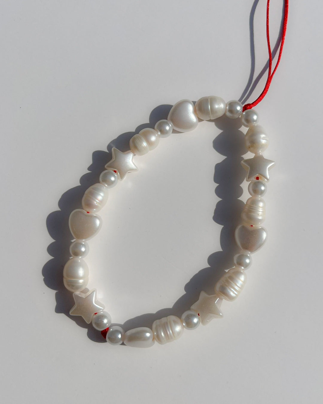 A studio shot of Buttercup Studio's Love Is In The Air Phone Strap. Made with white freshwater pearls and white star and heart shaped beads.