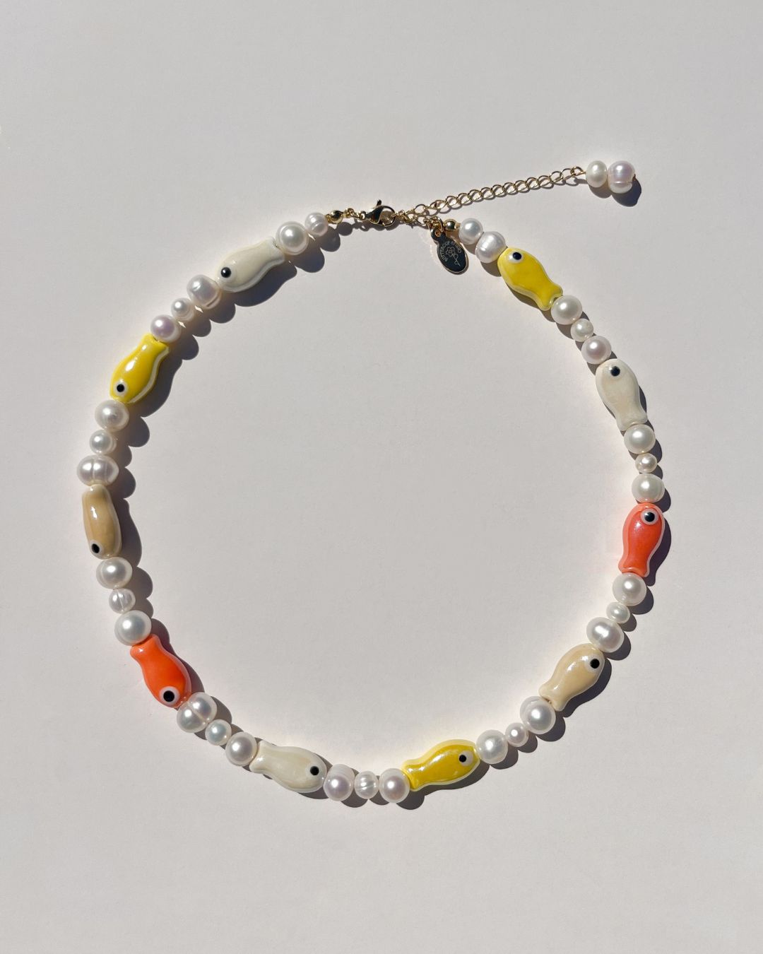 A close-up model shot of The Lucky Fish Freshwater Pearl Necklace is made using high quality rare AA+ freshwater pearls and glazed multi fish ceramic fish beads. Finished with 14k gold clasps and adjustable chain. This exclusive Buttercup Studio item is a limited edition and unisex. 