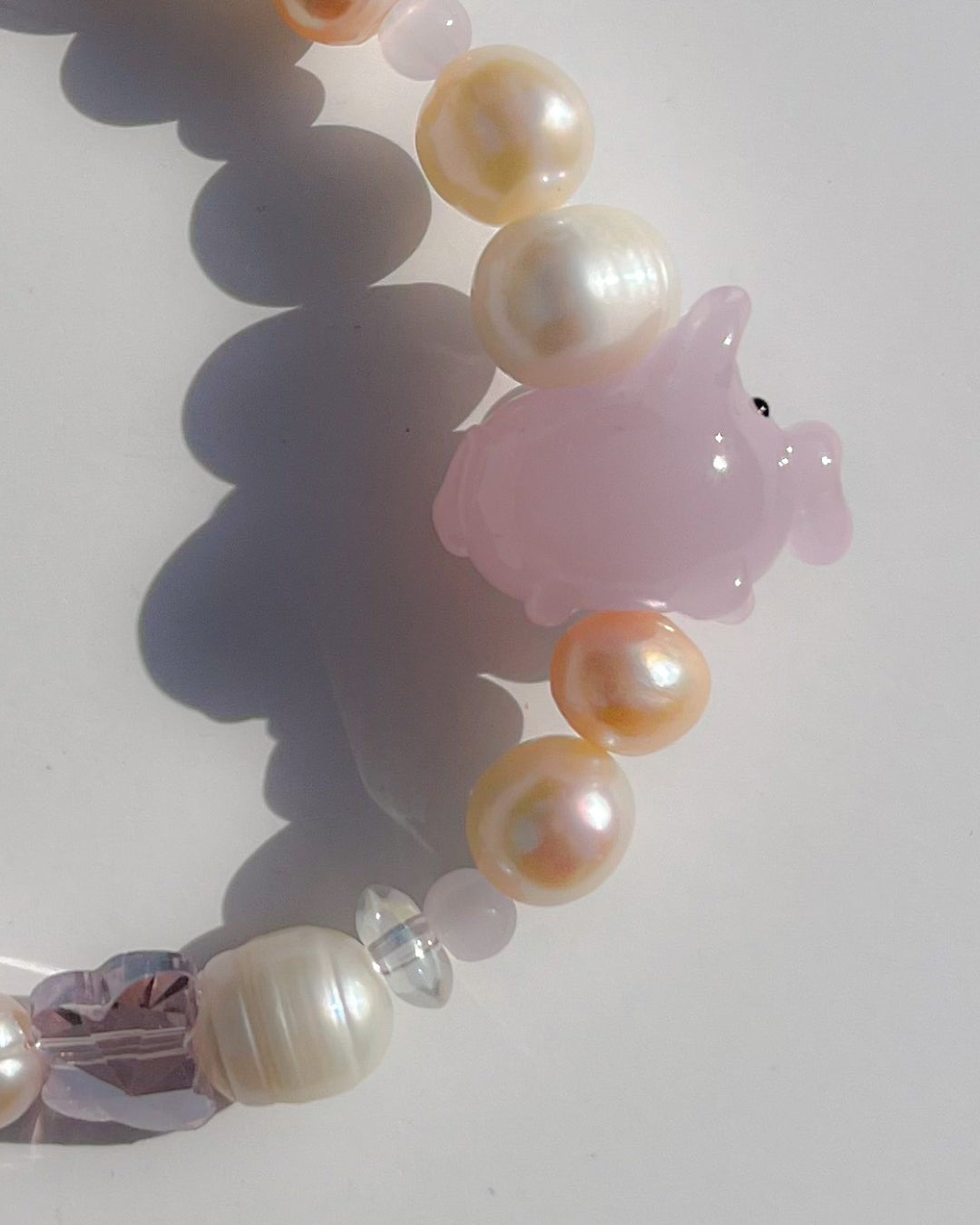 A close up studio shot of Buttercup Studio's Pink Piggie Freshwater Pearls Bracelet. Features assorted freshwater pearls, sheer pink beads and a special lampwork glass pink pig bead.