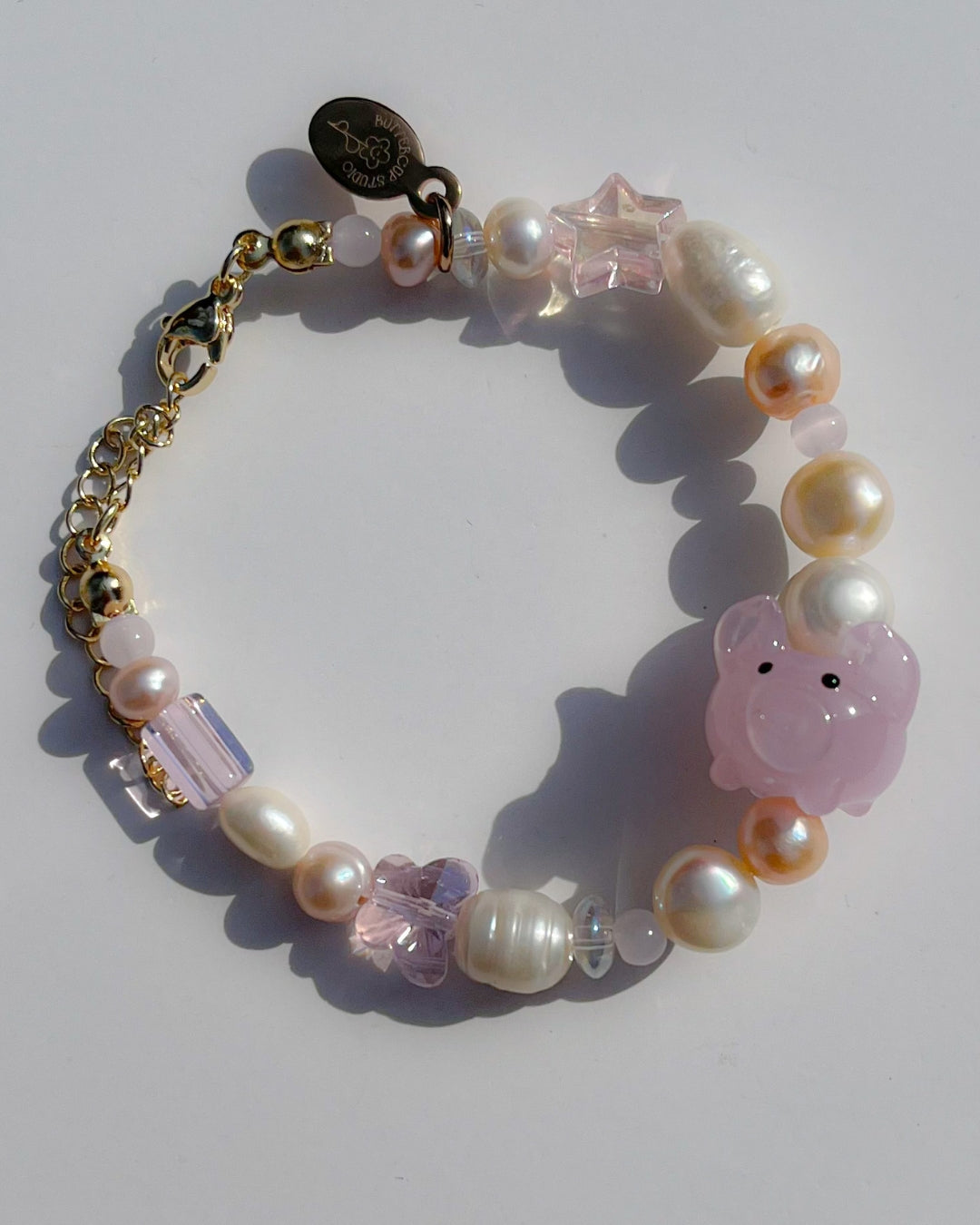 A studio shot of Buttercup Studio's Pink Piggie Freshwater Pearls Bracelet. Features assorted freshwater pearls, sheer pink beads and a special lampwork glass pink pig bead.