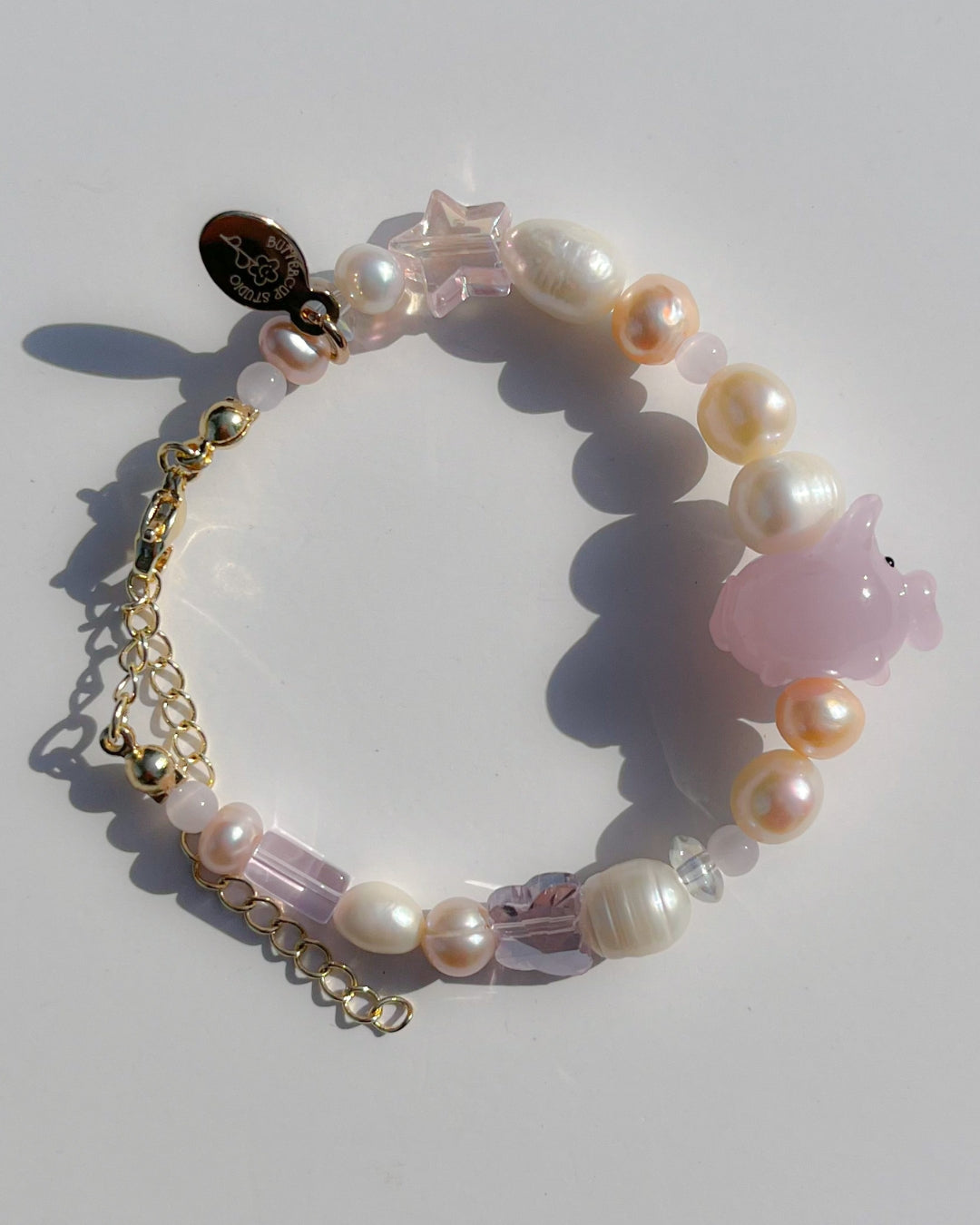 A studio shot of Buttercup Studio's Pink Piggie Freshwater Pearls Bracelet. Features assorted freshwater pearls, sheer pink beads and a special lampwork glass pink pig bead.