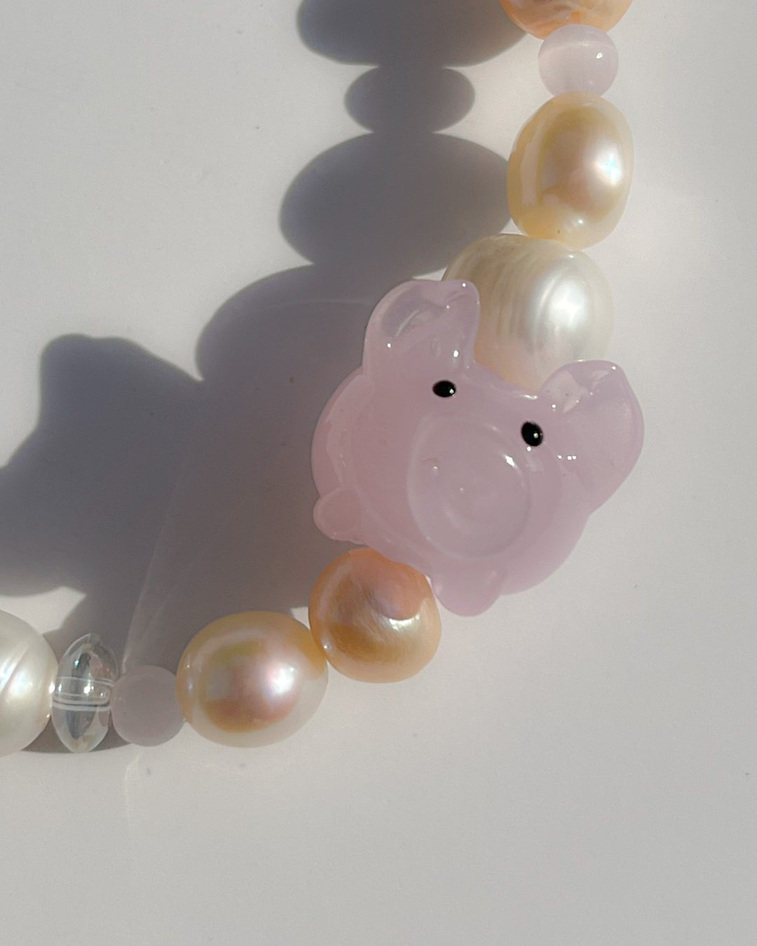 A close up studio shot of Buttercup Studio's Pink Piggie Freshwater Pearls Bracelet. Features assorted freshwater pearls, sheer pink beads and a special lampwork glass pink pig bead.