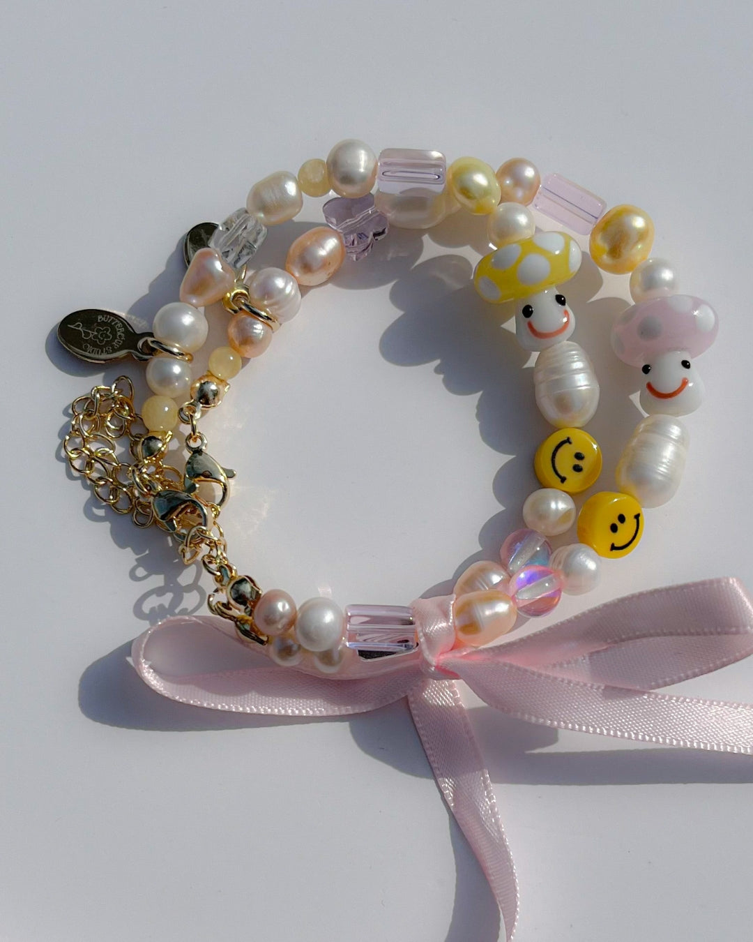 Both the Pink Shroomie Freshwater Pearls Bracelet and the Yellow Shroomie Freshwater Pearls Bracelet tied together with a pink bow.