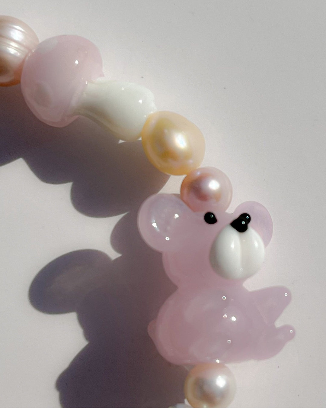 A close up studio shot of Buttercup Studio's Strawberry Beary Freshwater Pearls Bracelet. Made with assorted freshwater pearls, clear pink beads, a lampwork glass pink mushroom bead and a lampwork glass pink teddy bead.