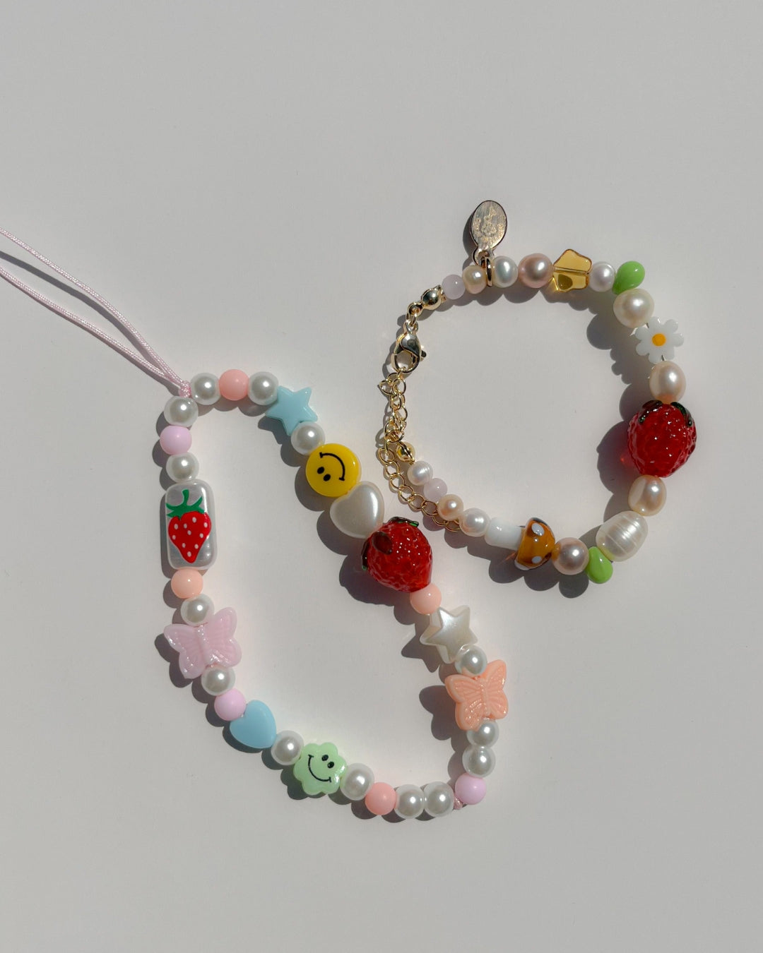 A studio shot of Buttercup Studio's Summertime Strawberry Freshwater Pearls Bracelet. Features assorted freshwater pearls, green and amber beads, a white daisy bead, a brown lampwork mushroom glass bead and a lampwork glass strawberry bead. 