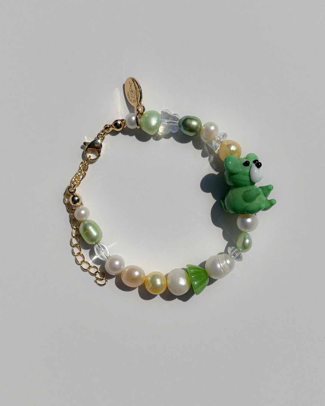 A studio shot of Buttercup Studio's Teddy Forest Garden Freshwater Pearls Bracelet. Made with assorted freshwater pearls, clear and green beads and a special lampwork glass green teddy bead.