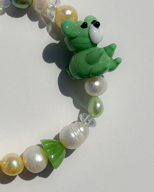 A close up studio shot of Buttercup Studio's Teddy Forest Garden Freshwater Pearls Bracelet. Made with assorted freshwater pearls, clear and green beads and a special lampwork glass green teddy bead.