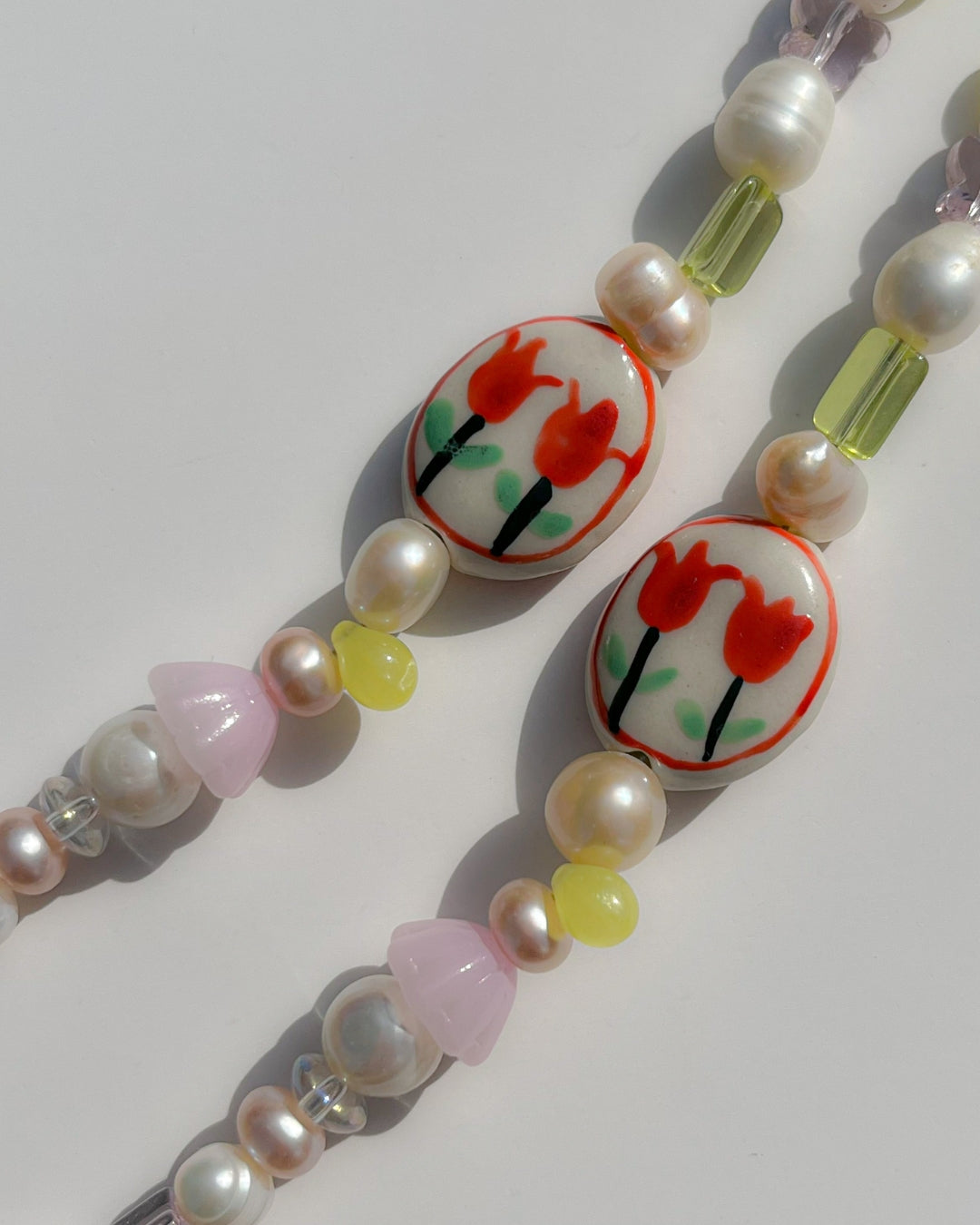 A studio shot of Buttercup Studio's Tulip Field Freshwater Pearls Bracelet. Made with assorted freshwater pearls, pink and yellow beads and a lampwork hand painted glass bead with two red tulips.