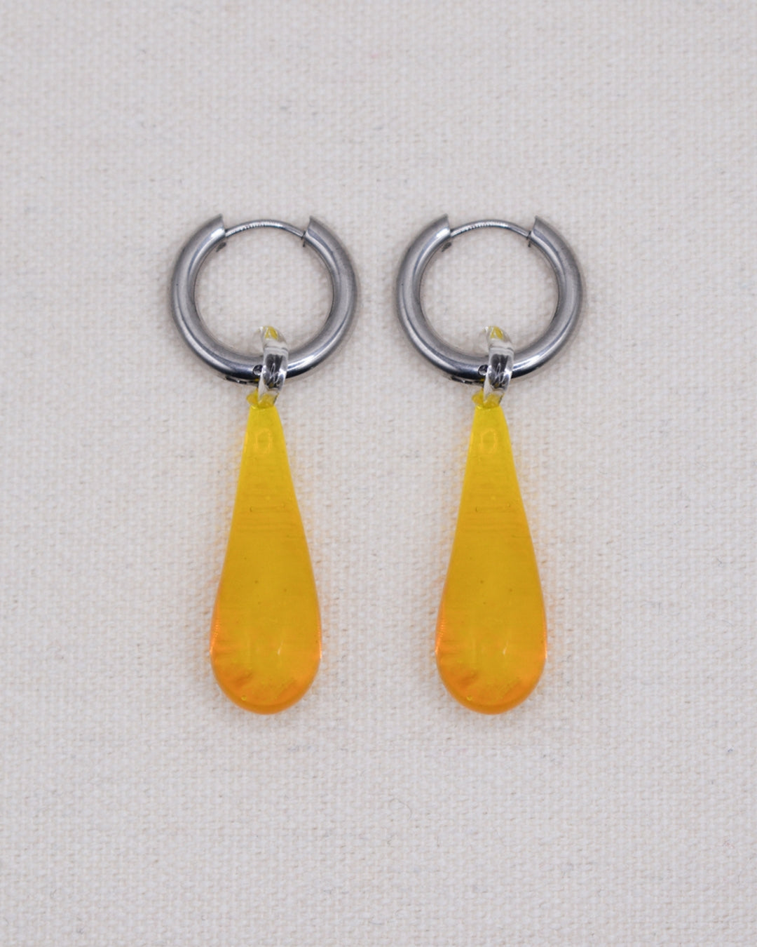 A studio shot of the Celeste earrings in honey from Buttercup Studio. The Celeste Earrings are made with thick 18k gold plated tarnish-resistant, hypoallergenic 12 mm thick hoops and high-quality 22mm lampwork glass water drop pendants.