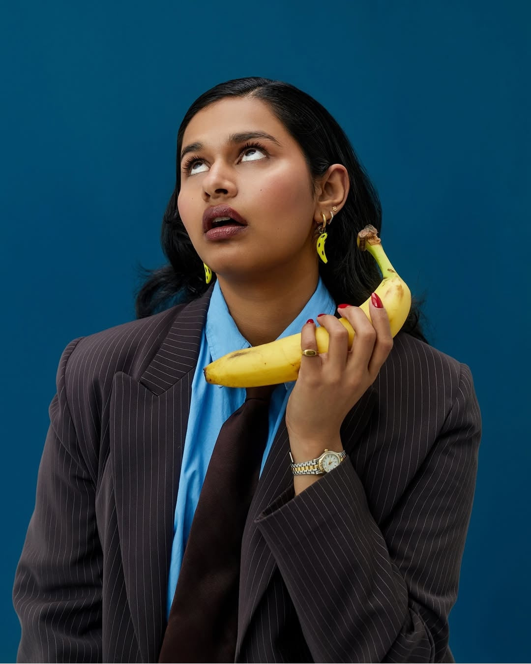 model wearing a pair of our statement The Banana Split Earrings. Features two handmade 30mm banana glass charms with gold-plated/sterling silver tarnish-resistant, 18k gold-plated stainless steel and hypoallergenic 12mm gold hoops.