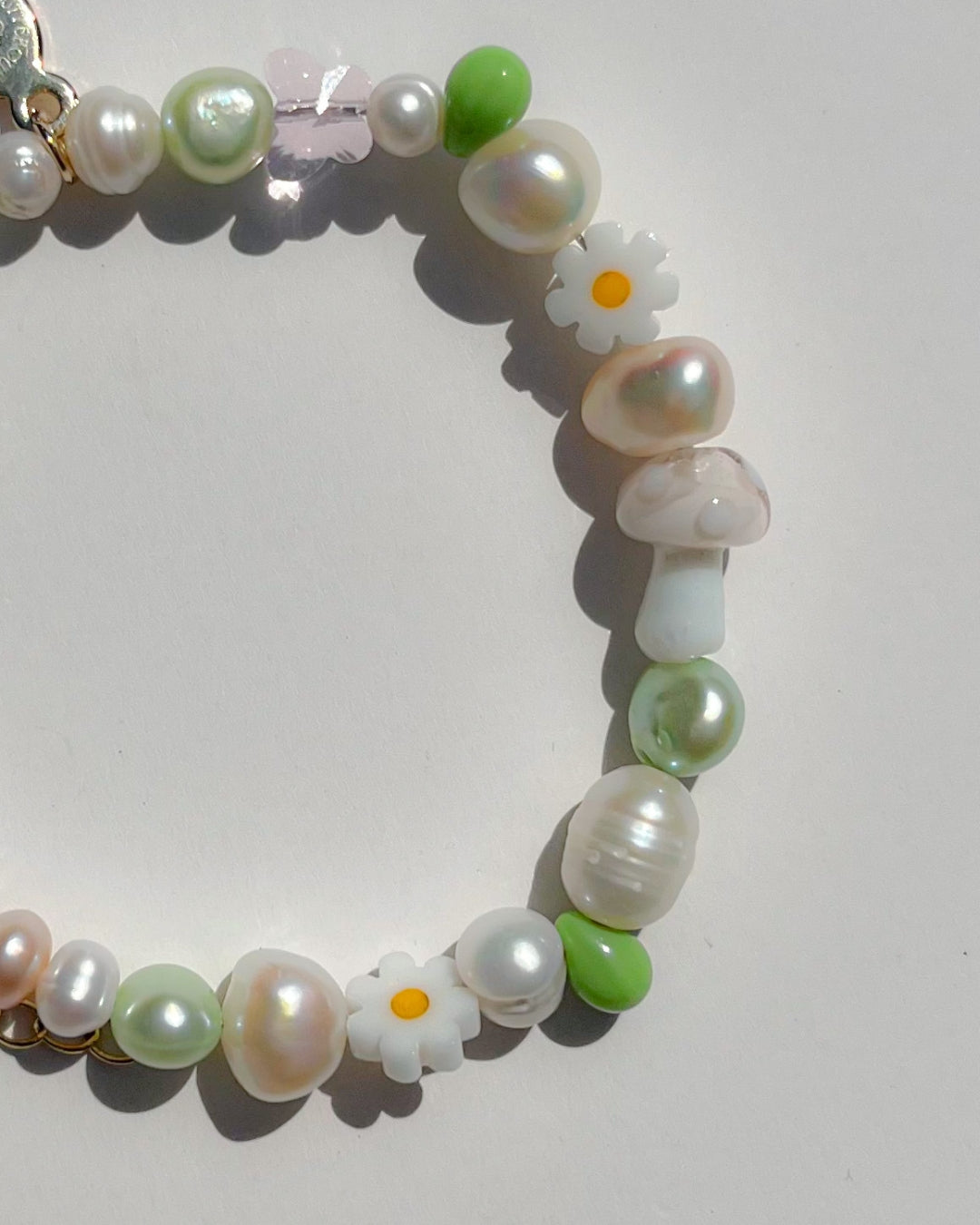 Studio shot of the Enchanted Freshwater Pearls Bracelet by Buttercup Studio. Features a white mushroom lampwork glass bead, daisy beads, green pearls and beads, and assorted freshwater pearls.