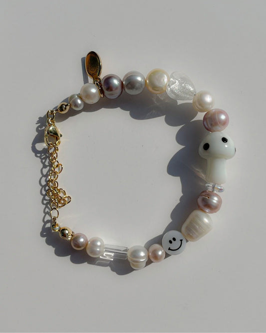 A studio shot of Buttercup Studio's Frosty Shroom Freshwater Pearls Bracelet. Made with pink, white, silver and yellow freshwater pearls, sparkly silver beads, clear beads, a white smiley face bead and a special white mushroom lampwork glass bead.