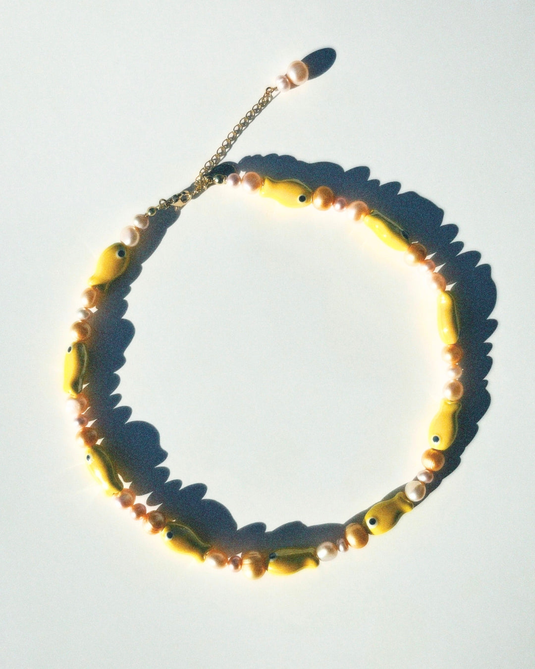 A close-up model shot of The Lucky Fish Freshwater Pearl Necklace in banana yellow is made using high-quality AA+ freshwater pearls and glazed fish ceramic fish beads. Finished with 14k gold clasps and an adjustable chain. This exclusive Buttercup Studio item is a limited edition and unisex.