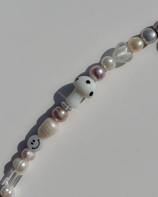 A close up studio shot of Buttercup Studio's Frosty Shroom Freshwater Pearls Bracelet. Made with pink, white, silver and yellow freshwater pearls, sparkly silver beads, clear beads, a white smiley face bead and a special white mushroom lampwork glass bead. 