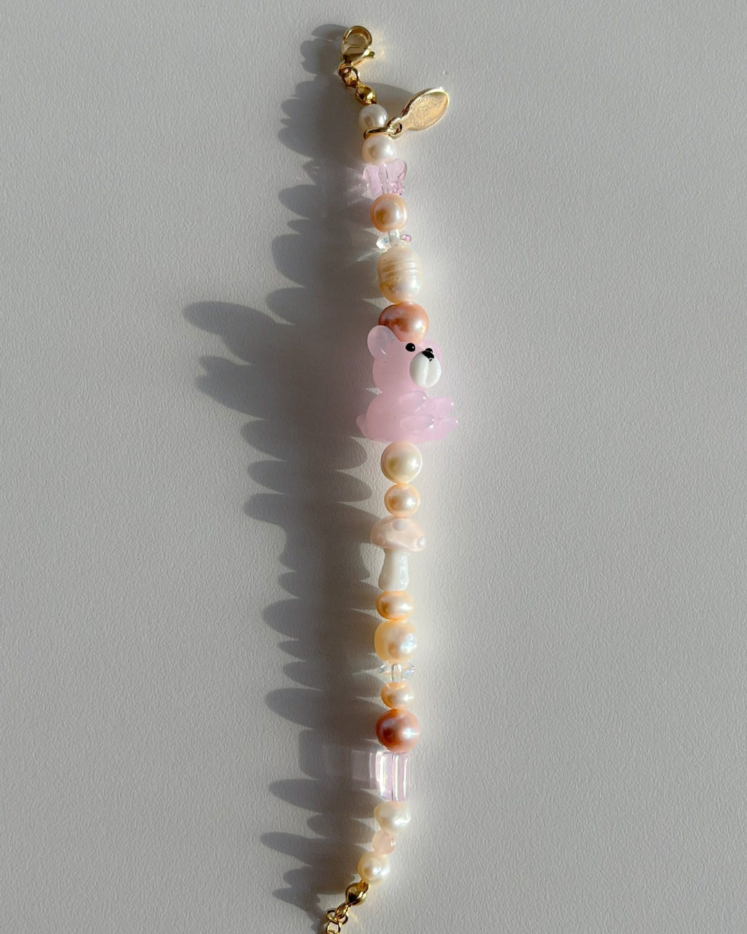 A studio shot of Buttercup Studio's Honey Bear Freshwater Pearls Bracelet. Made with assorted freshwater pearls, clear pink beads, a special pink mushroom lampwork glass bead and a special pink teddy lampwork glass bead.