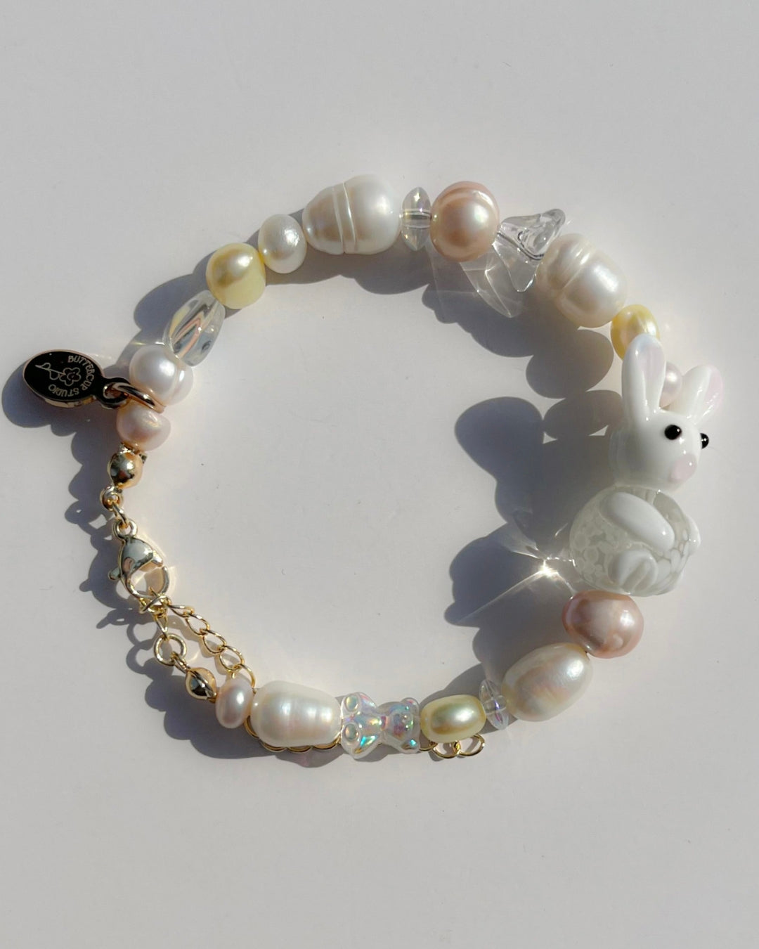 A close up studio shot of Buttercup Studio's Honey Bunny Freshwater Pearls Bracelet. Made with assorted freshwater pearls, clear beads and a special white bunny lampwork glass bead.