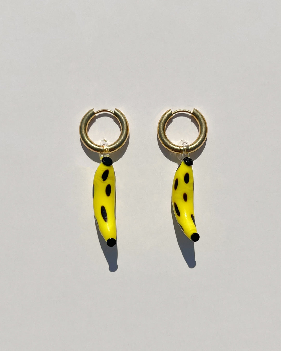 model wearing a pair of our statement The Banana Split Earrings. Features two handmade 30mm banana glass charms with gold-plated/sterling silver tarnish-resistant, 18k gold-plated stainless steel and hypoallergenic 12mm gold hoops.