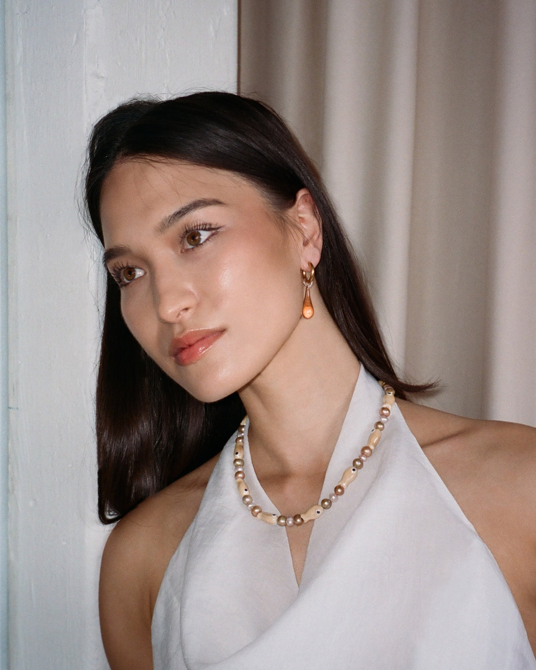 A close-up model shot of The Lucky Fish Freshwater Pearl Necklace is made using high quality AA+ rare brown hue freshwater pearls and glazed beige fish ceramic fish beads. Finished with 14k gold clasps and adjustable chain. This exclusive Buttercup Studio item is a limited edition and unisex.