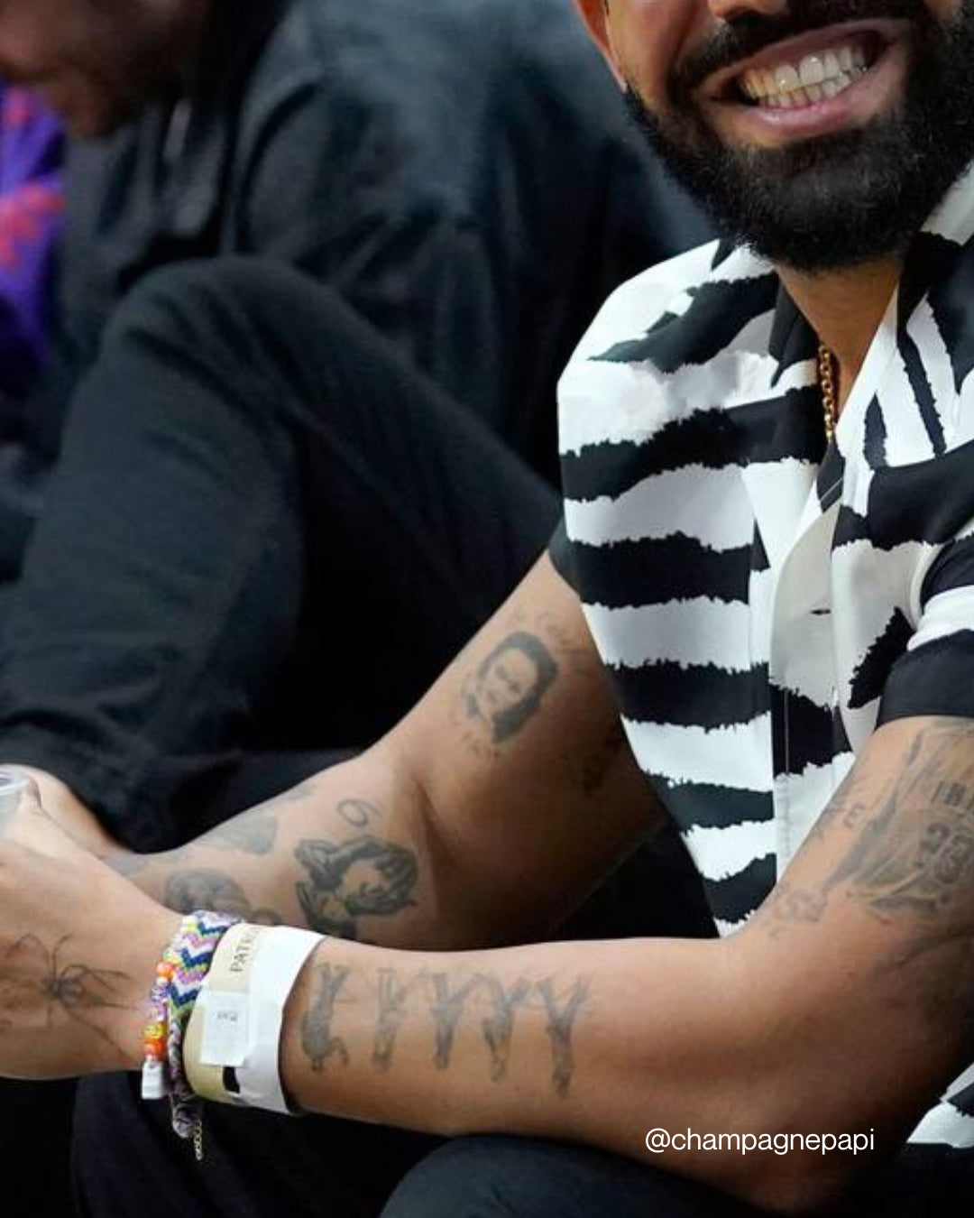 A close up of Drake seated at a sports event wearing a Custom Multi Colour Bracelet by Buttercup Studio. Image credits @champagnepapi on Instagram.