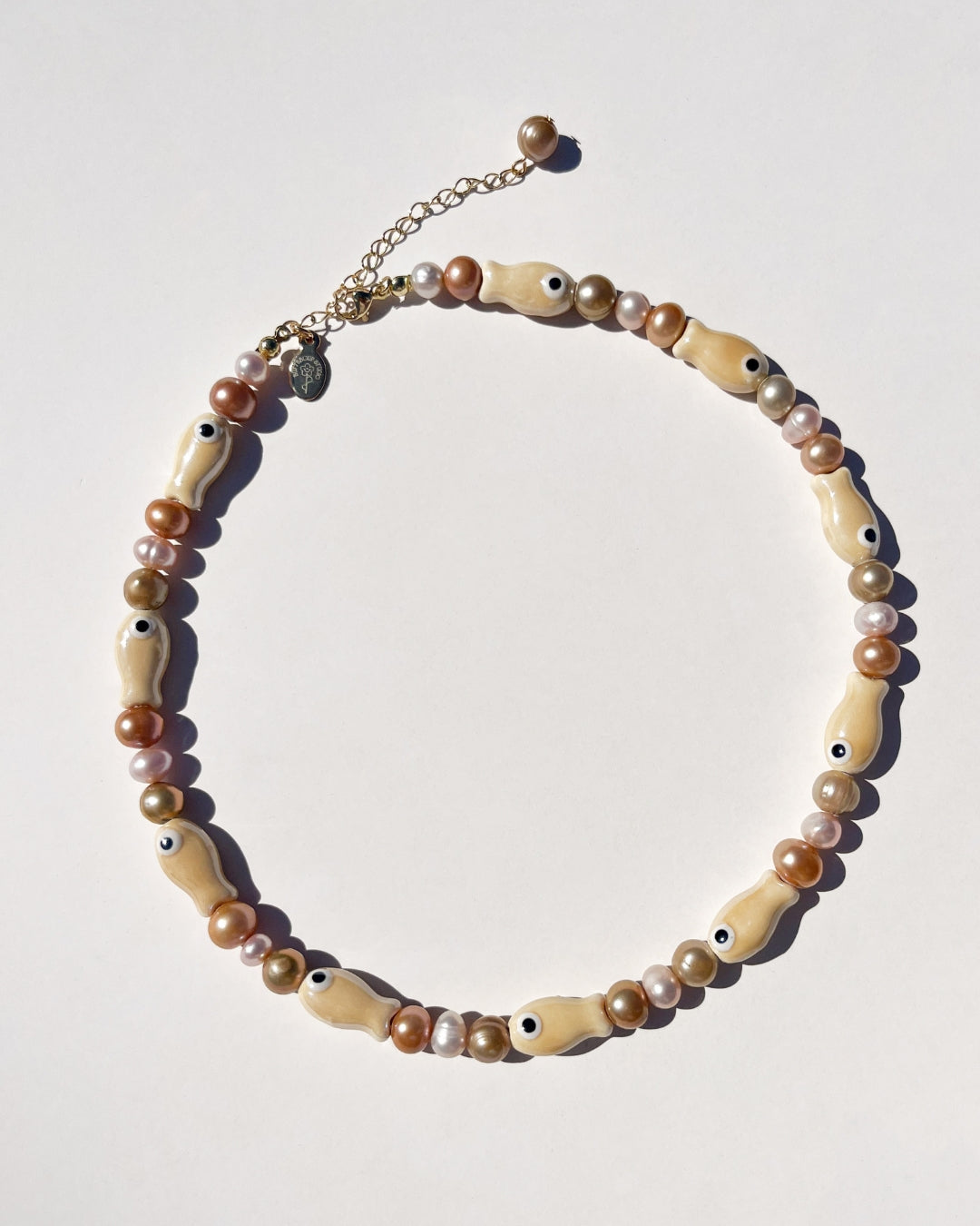 A close-up model shot of The Lucky Fish Freshwater Pearl Necklace is made using high quality AA+ rare brown hue freshwater pearls and glazed beige fish ceramic fish beads. Finished with 14k gold clasps and adjustable chain. This exclusive Buttercup Studio item is a limited edition and unisex.