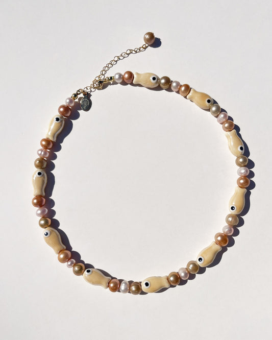 Shot of The Lucky Fish Freshwater Pearl Necklace is made using high quality AA+ rare brown hue freshwater pearls and glazed beige fish ceramic fish beads. Finished with 14k gold clasps and adjustable chain. This exclusive Buttercup Studio item is a limited edition and unisex.